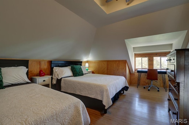 bedroom with wood finished floors, a wainscoted wall, wooden walls, and vaulted ceiling