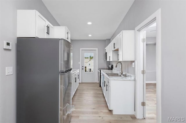 kitchen featuring appliances with stainless steel finishes, a sink, light wood-style floors, light countertops, and white cabinets