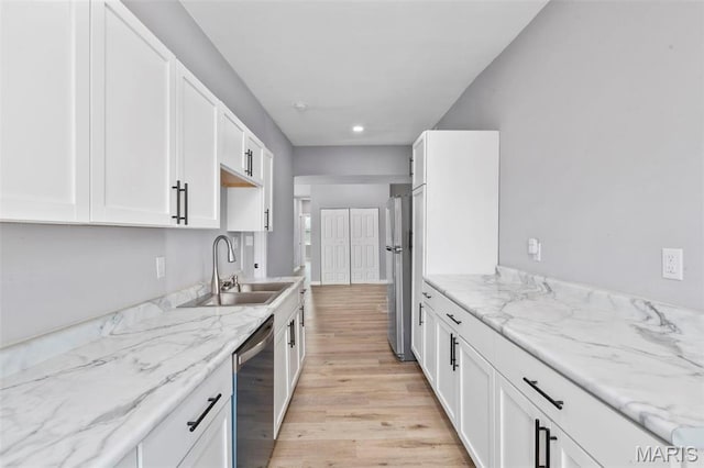 kitchen featuring stainless steel appliances, a sink, light wood-style floors, white cabinetry, and light stone counters