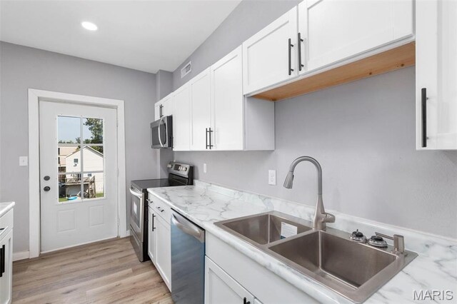kitchen featuring stainless steel appliances, a sink, white cabinets, recessed lighting, and light wood finished floors