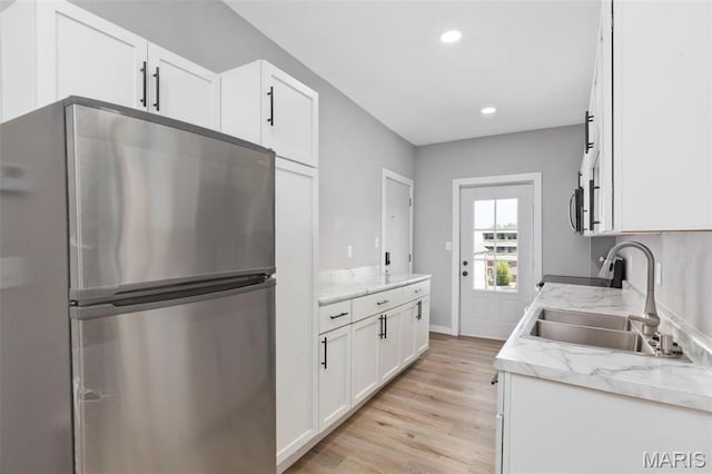kitchen with appliances with stainless steel finishes, a sink, light wood finished floors, white cabinetry, and recessed lighting