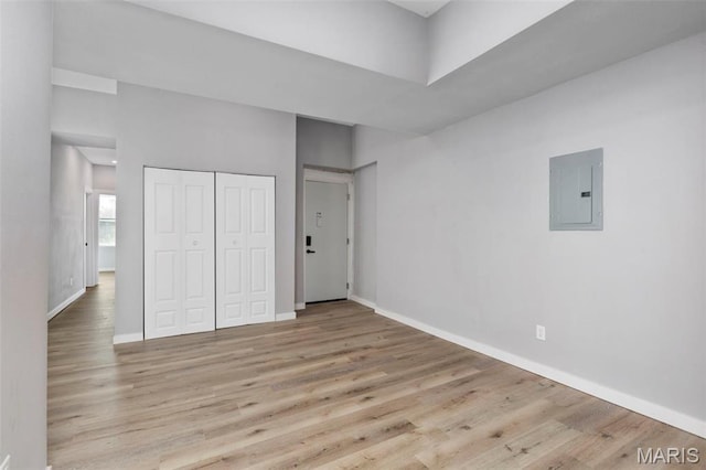 unfurnished bedroom with electric panel, wood finished floors, baseboards, and a closet