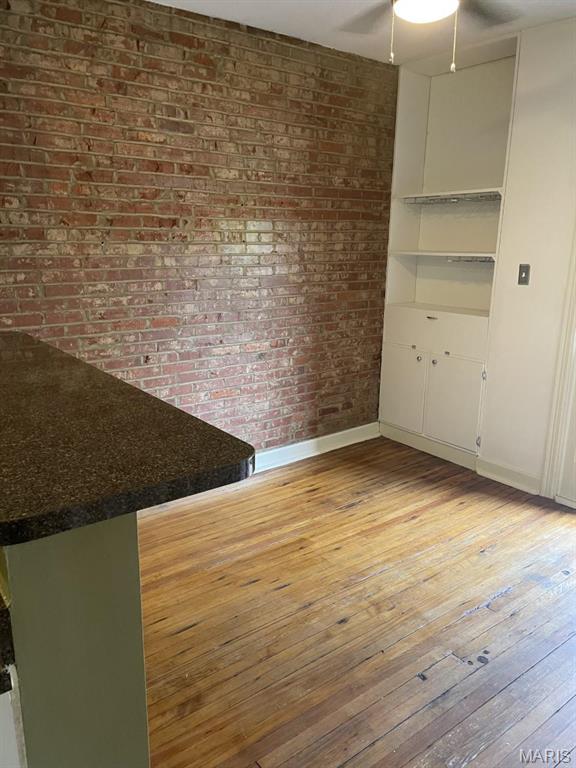 unfurnished dining area with light wood-style flooring, brick wall, a ceiling fan, and baseboards