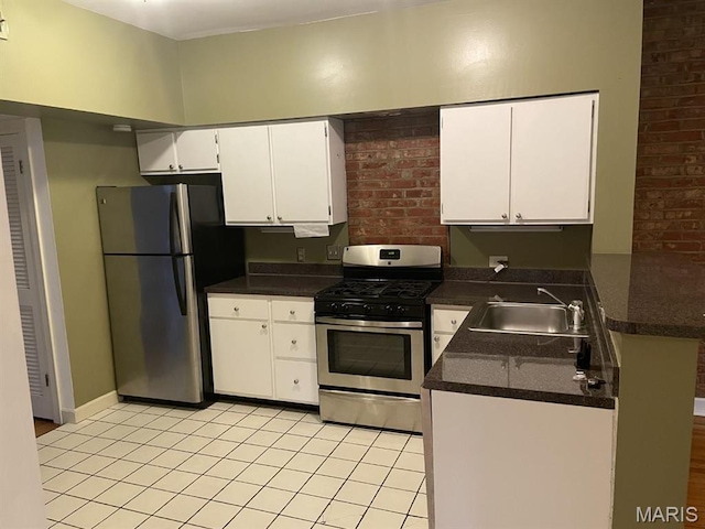 kitchen with appliances with stainless steel finishes, a sink, light tile patterned floors, dark countertops, and white cabinets