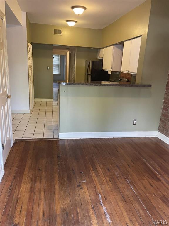 kitchen with freestanding refrigerator, white cabinets, hardwood / wood-style flooring, a peninsula, and baseboards