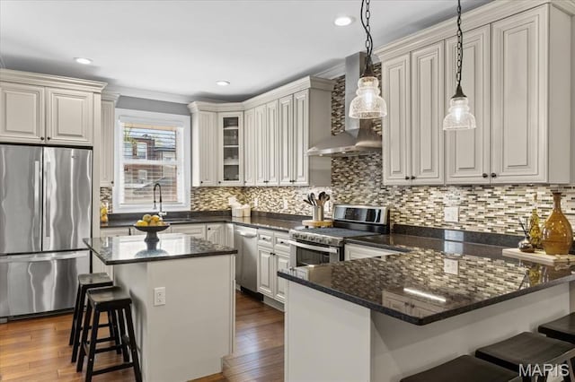 3884 Wyoming St, Saint Louis, MO 63116 - kitchen featuring appliances with stainless steel finishes, wall chimney range hood, a peninsula, a breakfast bar, and decorative backsplash