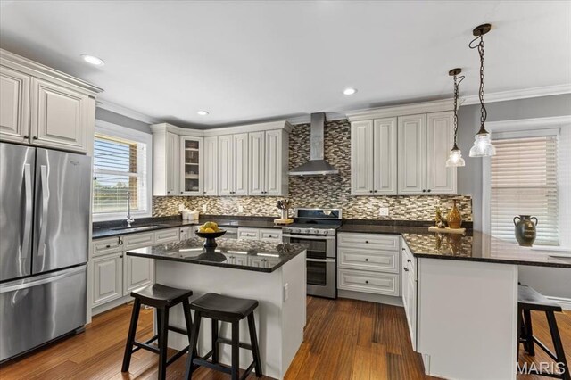 3884 Wyoming St, Saint Louis, MO 63116 - kitchen featuring appliances with stainless steel finishes, wall chimney range hood, a sink, a breakfast bar, and crown molding