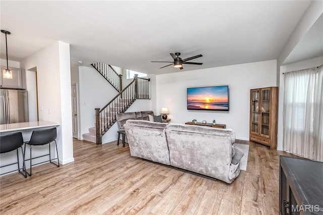 living area with a ceiling fan, light wood-style floors, stairs, and baseboards