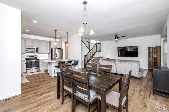 dining room featuring light wood-style flooring, a chandelier, a ceiling fan, stairway, and recessed lighting