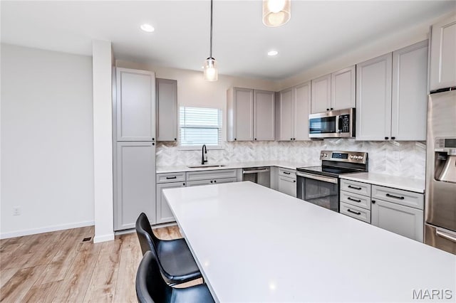 kitchen with appliances with stainless steel finishes, a sink, gray cabinetry, decorative backsplash, and recessed lighting