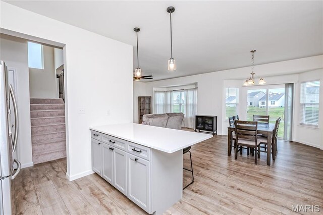 kitchen featuring freestanding refrigerator, light wood finished floors, a peninsula, light countertops, and a breakfast bar