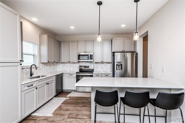 kitchen with appliances with stainless steel finishes, a peninsula, a sink, a breakfast bar, and light wood-style flooring
