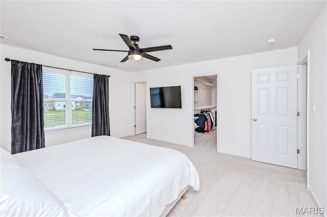 bedroom with light colored carpet, a walk in closet, baseboards, and ceiling fan