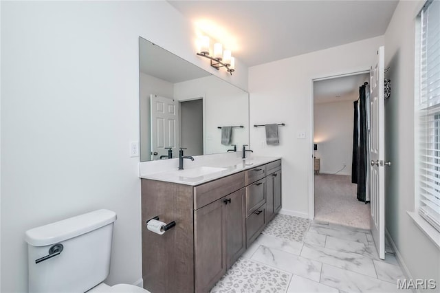 bathroom featuring marble look tiles, double vanity, toilet, and baseboards