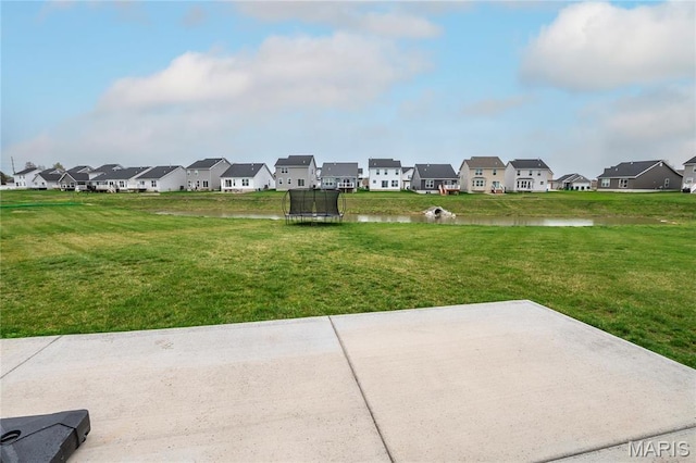 view of grassy yard featuring a trampoline, a residential view, a patio area, and a water view