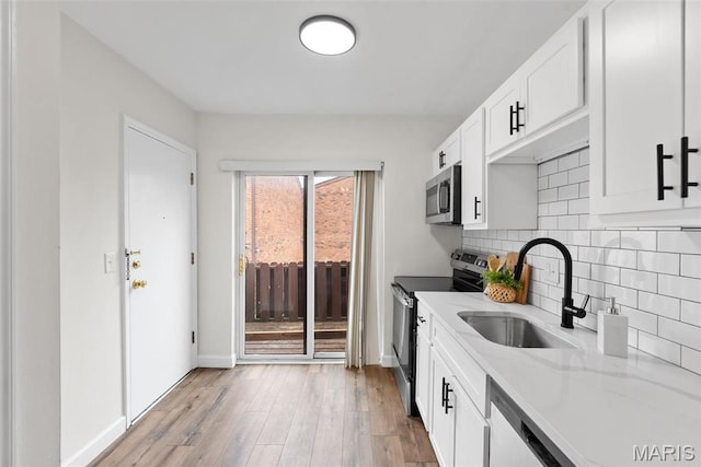 kitchen featuring stainless steel appliances, a sink, tasteful backsplash, light wood-style flooring, and baseboards