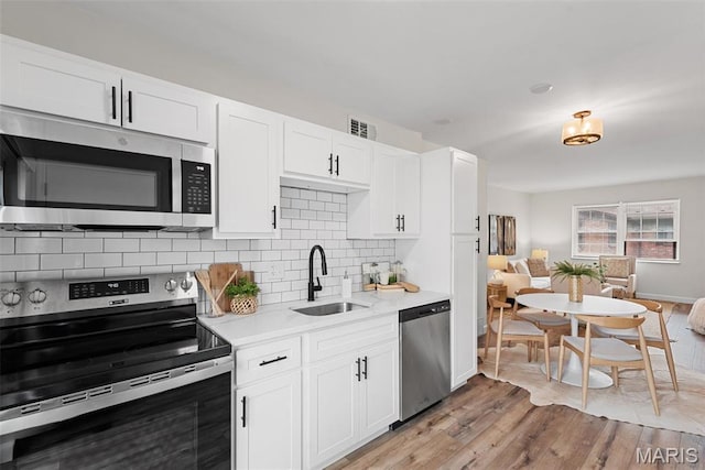 kitchen featuring stainless steel appliances, a sink, light countertops, decorative backsplash, and light wood-type flooring