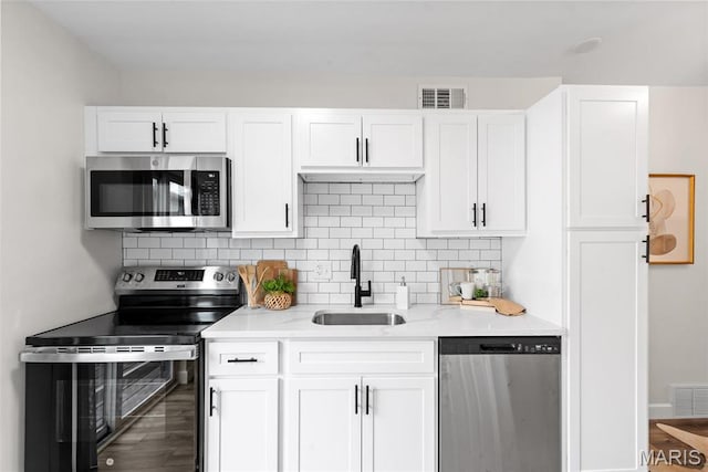 kitchen with appliances with stainless steel finishes, a sink, white cabinetry, decorative backsplash, and wood finished floors