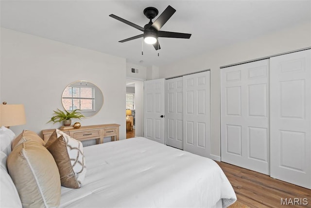 bedroom featuring two closets, wood finished floors, and ceiling fan