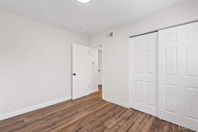 unfurnished bedroom with wood finished floors, baseboards, and a closet
