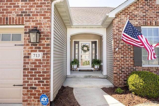 doorway to property featuring brick siding, a garage, and roof with shingles