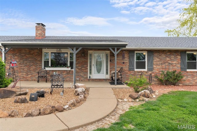 ranch-style house with brick siding, a chimney, a shingled roof, and covered porch