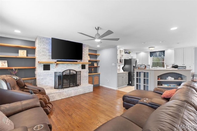 living area with ceiling fan, light wood-style floors, recessed lighting, ornamental molding, and a fireplace