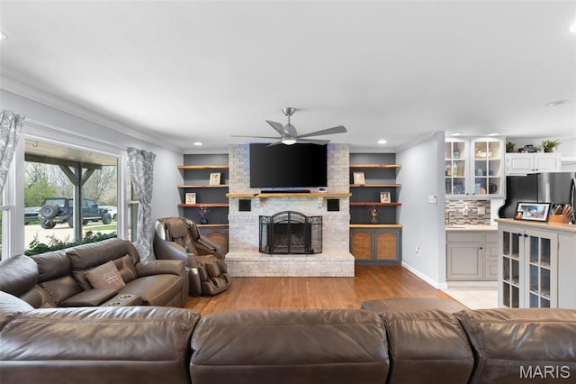living area with light wood-type flooring, a ceiling fan, ornamental molding, a brick fireplace, and recessed lighting