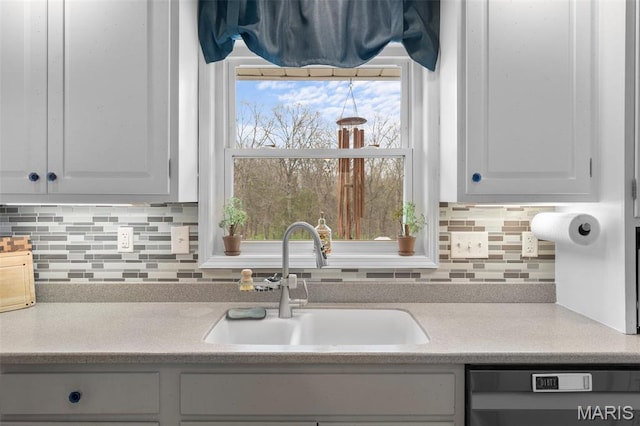 kitchen with black dishwasher, a sink, light countertops, backsplash, and white cabinets