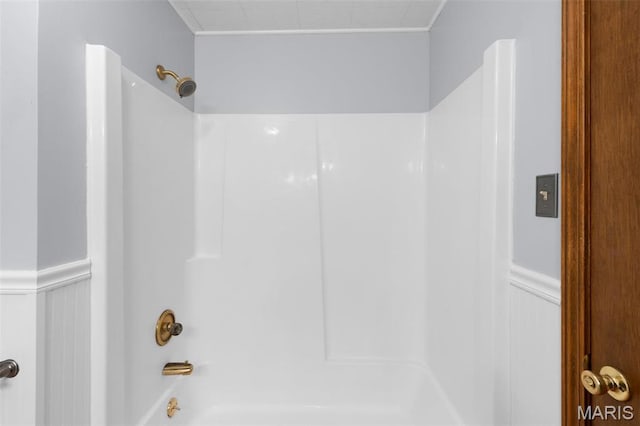 bathroom with bathtub / shower combination, a wainscoted wall, and a decorative wall