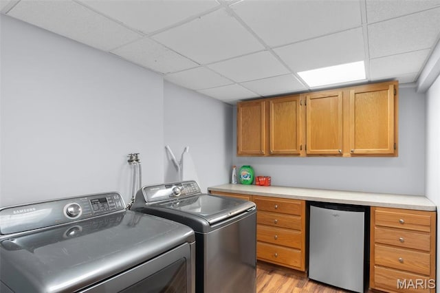 washroom with washing machine and dryer, light wood-style flooring, and cabinet space