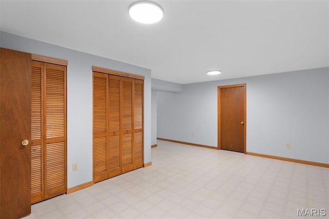 unfurnished bedroom featuring two closets, baseboards, and light floors