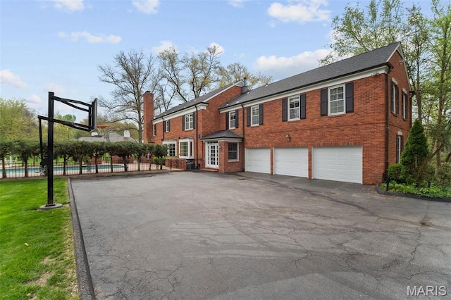 21 Log Cabin Dr, Saint Louis, MO 63124 - back of house featuring asphalt driveway, fence, brick siding, an attached garage, and a chimney