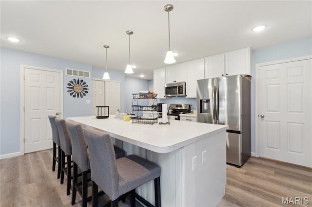 104 Tiber Way, Saint Charles, MO 63301 - kitchen featuring appliances with stainless steel finishes, light wood-type flooring, white cabinets, a kitchen island with sink, and recessed lighting