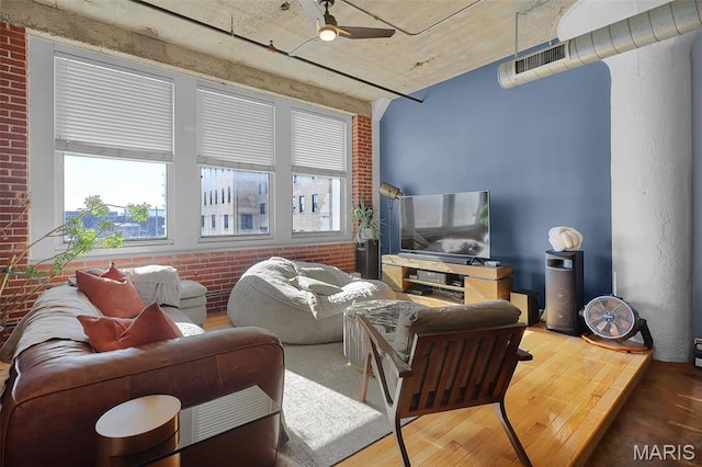 living room featuring wood finished floors, ceiling fan, and brick wall