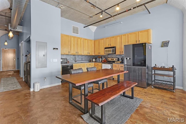 dining space featuring a towering ceiling, electric panel, concrete floors, and baseboards
