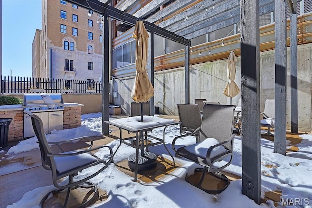snow covered patio with area for grilling, a grill, fence, and outdoor dining space