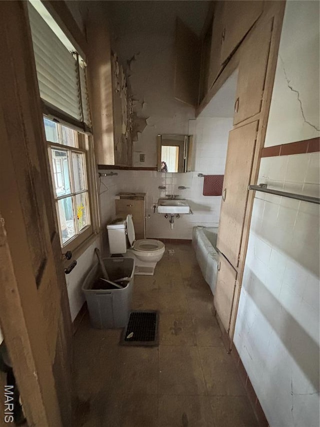 bathroom featuring toilet, tile walls, a sink, a wainscoted wall, and tile patterned flooring
