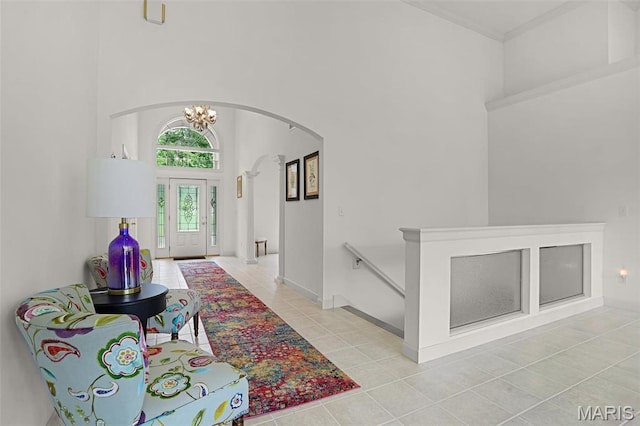 entrance foyer featuring arched walkways, a towering ceiling, light tile patterned floors, a chandelier, and baseboards