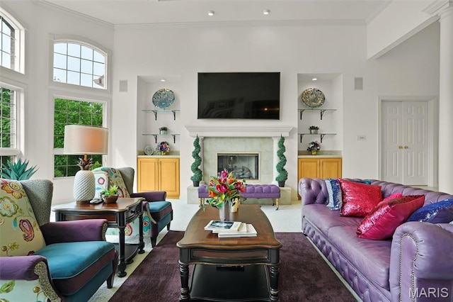 living room featuring built in shelves, carpet flooring, crown molding, and a glass covered fireplace