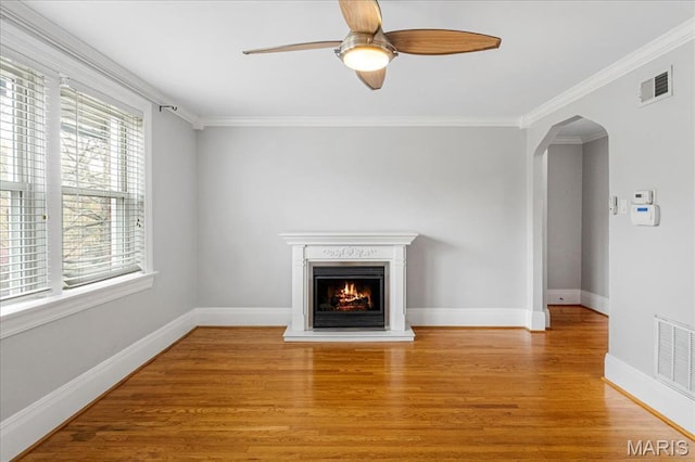 7570 Byron Pl Unit 3W, Saint Louis, MO 63105 - unfurnished living room featuring light wood-style flooring, a ceiling fan, a warm lit fireplace, ornamental molding, and arched walkways