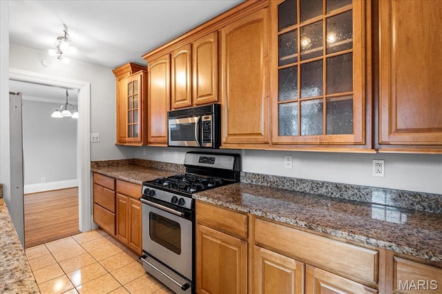 7570 Byron Pl Unit 3W, Saint Louis, MO 63105 - kitchen featuring stainless steel appliances, glass insert cabinets, dark stone countertops, light tile patterned floors, and a chandelier