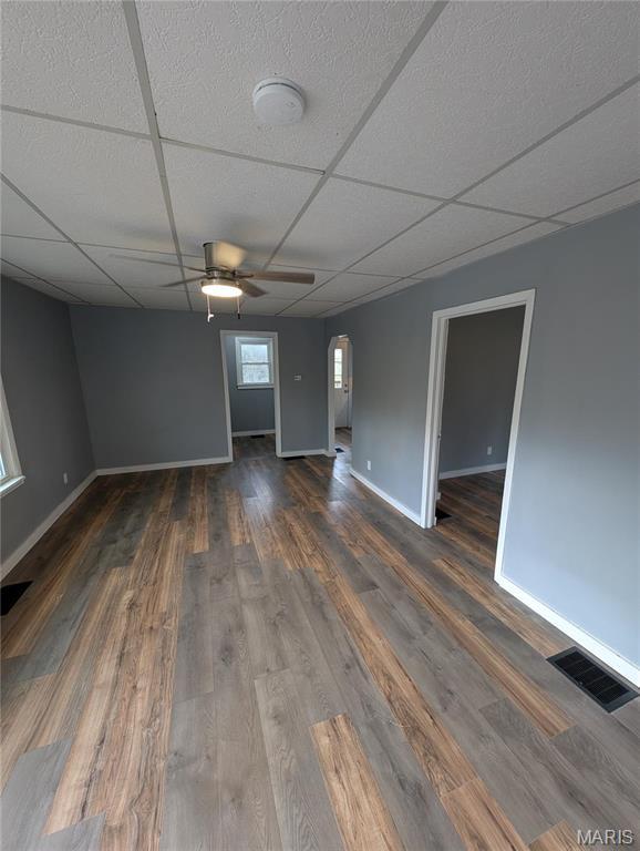 empty room with a ceiling fan, arched walkways, wood finished floors, baseboards, and a drop ceiling