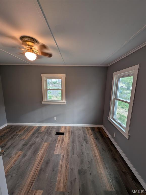 unfurnished room with healthy amount of natural light, crown molding, a ceiling fan, wood finished floors, and baseboards