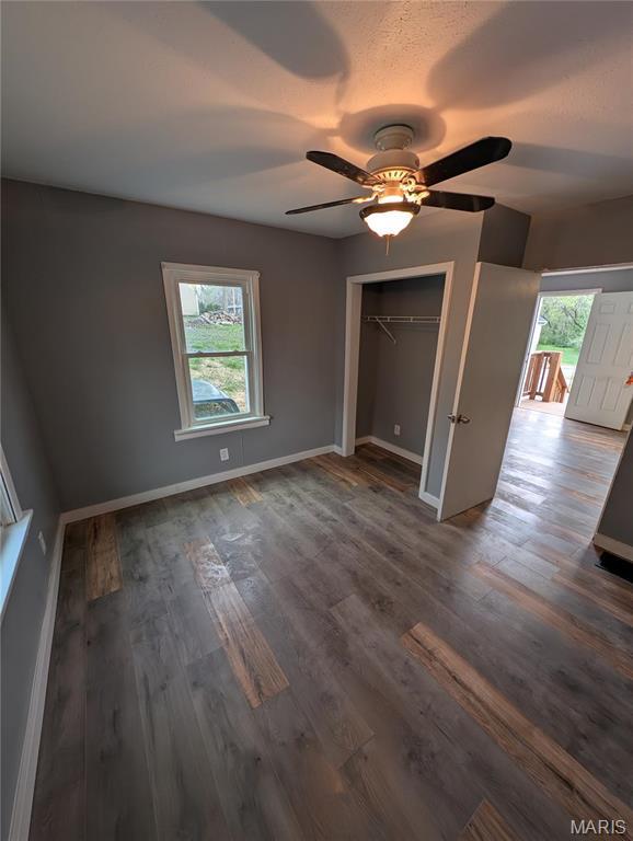 unfurnished bedroom featuring baseboards, a closet, dark wood-style floors, and a ceiling fan