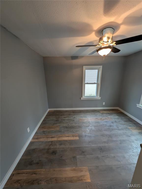 unfurnished room with a ceiling fan, baseboards, dark wood-style flooring, and a textured ceiling