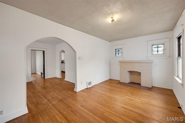 5923 Sherry Ave, Saint Louis, MO 63136 - unfurnished living room featuring light wood-style flooring, a fireplace, a textured ceiling, arched walkways, and baseboards