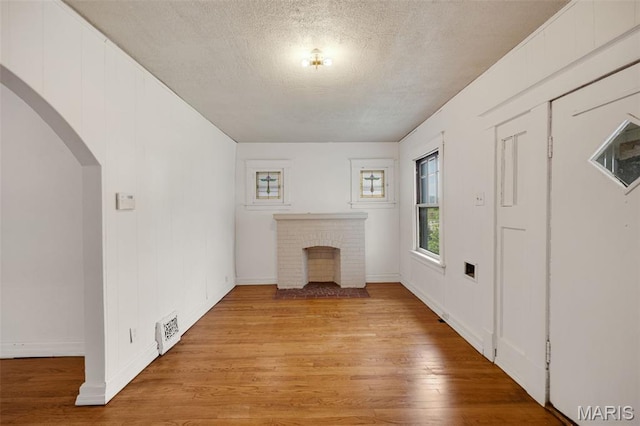 5923 Sherry Ave, Saint Louis, MO 63136 - unfurnished living room with light wood-style flooring, arched walkways, baseboards, a textured ceiling, and a fireplace