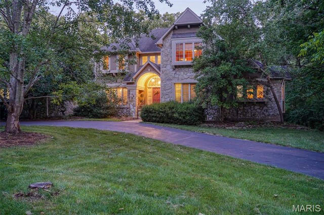 view of front facade featuring stone siding, a front lawn, and curved driveway