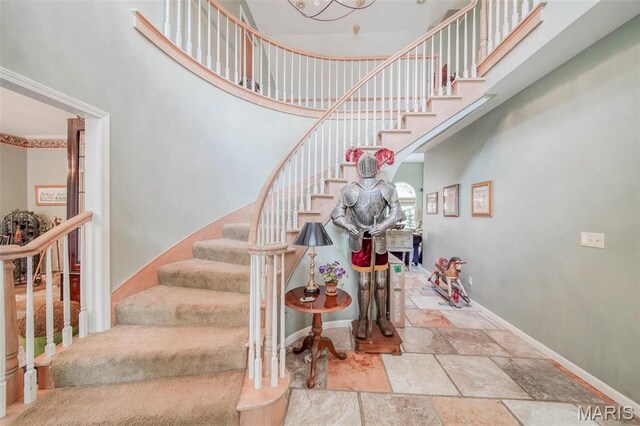 stairs with a towering ceiling, stone tile floors, and baseboards